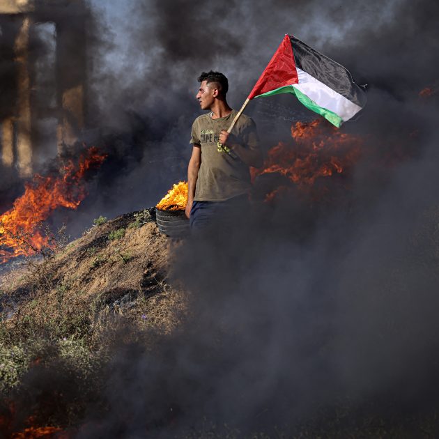 A Palestinian youth holds a flag next to burning tyres during a protest by the border fence with Israel east of Gaza City on July 3, 2023. Israel has stepped up operations in the northern West Bank, home to Jenin city and its adjacent refugee camp, a stronghold of Palestinian armed groups where there has been a spate of attacks on Israelis as well as attacks by Jewish settlers on Palestinian communities.