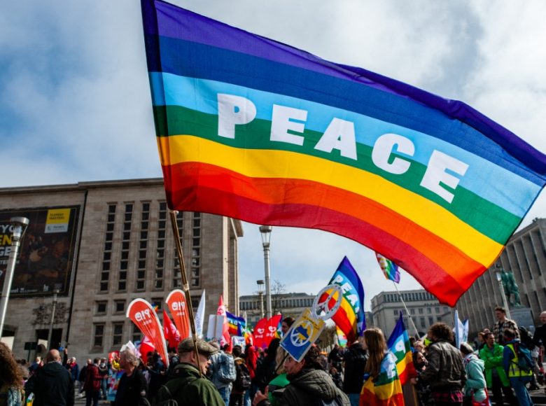 A man is holding a rainbow flag with the word Peace on it, during the National peace rally organized in Brussels, on March 27th, 2022. (Photo by Romy Arroyo Fernandez/NurPhoto) (Photo by Romy Arroyo Fernandez / NurPhoto / NurPhoto via AFP)