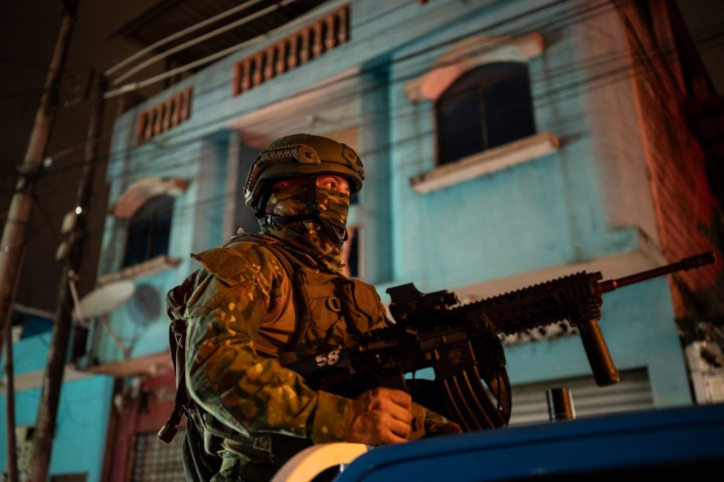 A soldier from the 5th Infantry Brigade keeps watch at the top of a pick-up truck during a security operation and search for suspects during the curfew, in a poor neighbourhood of Guayaquil, Ecuador, in the early hours of January 12, 2024. - Ecuador's armed forces were engaged in a brutal standoff with organized crime Thursday, deploying more than 22,400 soldiers to put down a campaign of terror waged by gangs that has claimed 16 lives.With an armed presence on the streets, patrols by land, sea and air, random body and car searches, prison raids and the enforcement of a curfew, the government of President Daniel Noboa has vowed not to yield in its "war" with 22 criminal gangs. (Photo by Yuri CORTEZ / AFP)