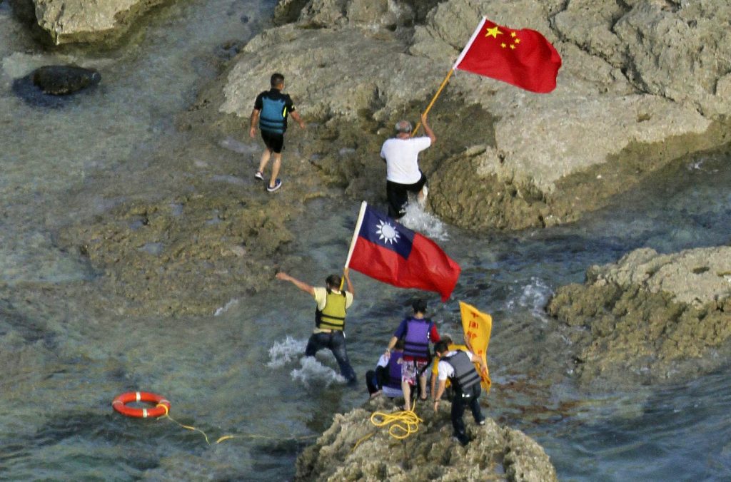 In a photograph taken on August 15, 2012, pro-China activists carrying Chinese and Taiwanese national flags walk on the disputed island known as Senkaku in Japan and Diaoyu in China after arriving on their boat, west of Japan's sourthern island of Okinawa. Taiwan on August 16 urged Japan to release a group of pro-China activists arrested for landing on a disputed island in the East China Sea on August 15. AFP PHOTO / YOMIURI SHIMBUN JAPAN OUT (Photo by Yomiuri Shimbun / AFP)