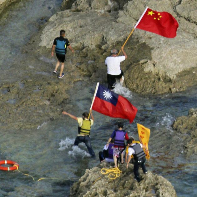 In a photograph taken on August 15, 2012, pro-China activists carrying Chinese and Taiwanese national flags walk on the disputed island known as Senkaku in Japan and Diaoyu in China after arriving on their boat, west of Japan's sourthern island of Okinawa. Taiwan on August 16 urged Japan to release a group of pro-China activists arrested for landing on a disputed island in the East China Sea on August 15. AFP PHOTO / YOMIURI SHIMBUN JAPAN OUT (Photo by Yomiuri Shimbun / AFP)