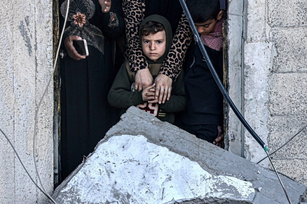 A child looks on while standing with others through the doorway of a room adjacent to a destroyed building, in the aftermath of Israeli bombardment on Rafah in the southern Gaza Strip on February 7, 2024, amid the ongoing conflict between Israel and the Palestinian militant group Hamas. (Photo by SAID KHATIB / AFP)