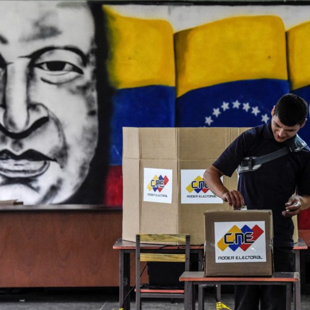 A man casts his vote in front of an image of late Venezuelan president Hugo Chavez, during the presidential elections at a polling station in Caracas on May 20, 2018. Venezuelans, reeling under a devastating economic crisis, began voting Sunday in an election boycotted by the opposition and condemned by much of the international community but expected to hand deeply unpopular President Nicolas Maduro a new mandate (Photo by Juan BARRETO / AFP)