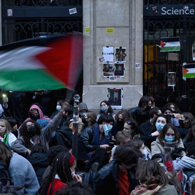 A protestor waves a Palestinian flag as they stage a sit-in in front of French riot policemen near the entrance of a Institute of Political Studies (Sciences Po Paris) building occupied by students, in Paris on April 26, 2024. - Students occupied a new building at Sciences Po Paris, in support of Palestinians, a day after police evacuated another of the school's sites, echoing protest action at American universities. (Photo by JULIEN DE ROSA / AFP)