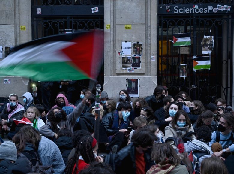 A protestor waves a Palestinian flag as they stage a sit-in in front of French riot policemen near the entrance of a Institute of Political Studies (Sciences Po Paris) building occupied by students, in Paris on April 26, 2024. - Students occupied a new building at Sciences Po Paris, in support of Palestinians, a day after police evacuated another of the school's sites, echoing protest action at American universities. (Photo by JULIEN DE ROSA / AFP)