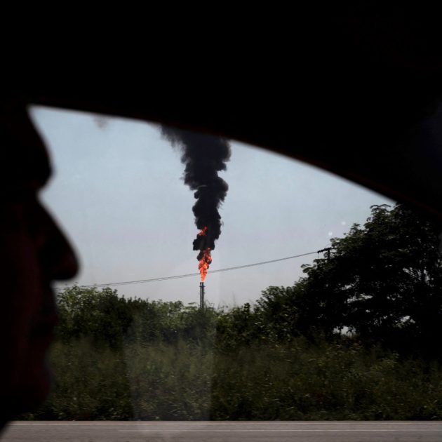 A driver drives his vehicle along the road in front of a burning degassing chimney at an oil and gas plant in Puerto La Cruz, Anzoategui State, Venezuela, on September 11, 2023. (Photo by Yuri CORTEZ / AFP)