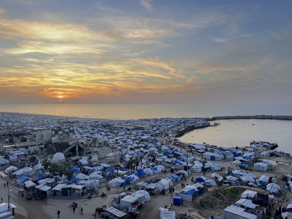 An aerial view shows displaced Palestinians living in makeshift shelters among the ruins of destroyed buildings along the coastline of Gaza City in the Gaza Strip on January 6, 2026. The war has devastated large parts of Gaza City, leaving much of the population displaced and reliant on temporary shelters. (Photo by Hassan Salem / Middle East Images via AFP)