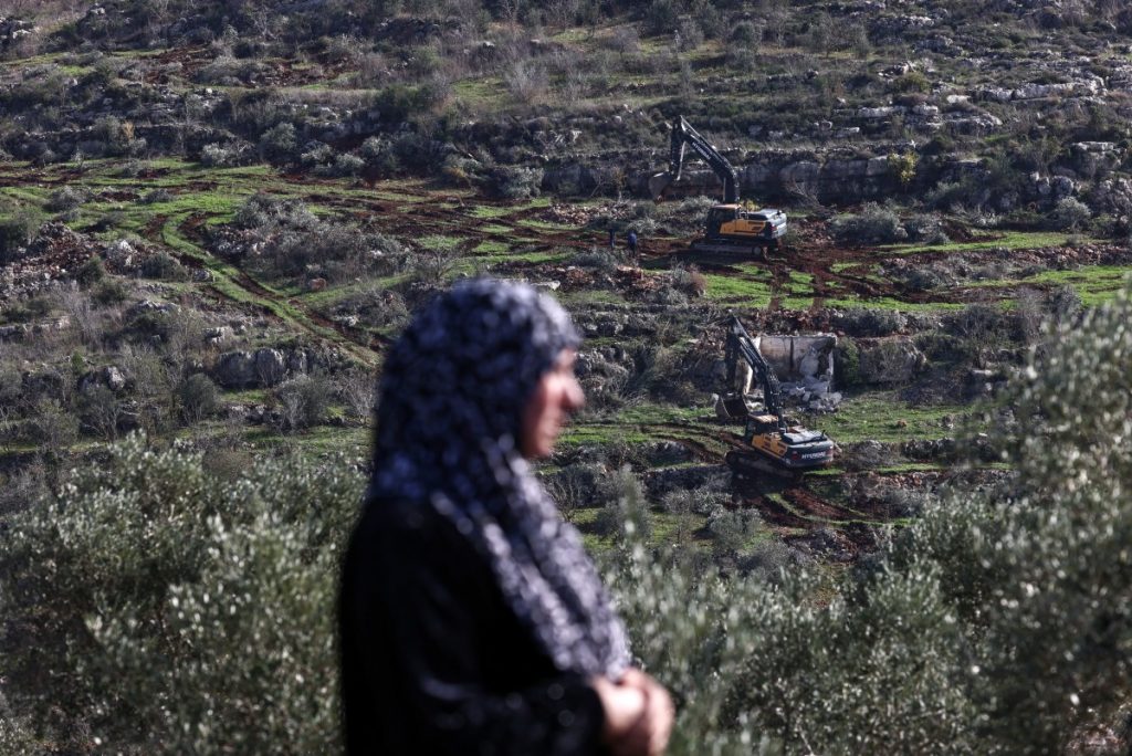 A Palestinian woman, Etaf jaradat from Silat al-Harithiya, watches from a hill as Israeli bulldozers work on her land to reportedly make way for the construction of settlements in the Sarouj area, located between the towns of Silat al-Harithiya and Yamoun, west of Jenin in the occupied west bank on December 22, 2025. Israel approved the establishment of 19 new settlements in the occupied West Bank, a move the far-right finance minister said on December 21 was aimed at preventing the establishment of a Palestinian state. (Photo by Zain JAAFAR / AFP)