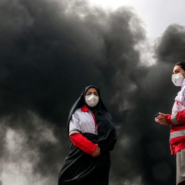 Women members of Iran's Red Crescent society stand near smoke plumes from an ongoing fire following an overnight airstrike on the Shahran oil refinery in northwestern Tehran on March 8, 2026. The United States and Israel launched strikes against Iran on February 28, sparking swift retaliation by the Islamic republic which responded with missile attacks across the region. The war has dragged in global powers, upended the world's energy and transport sectors, and brought chaos to even usually peaceful areas of the volatile region. (Photo by AFP)