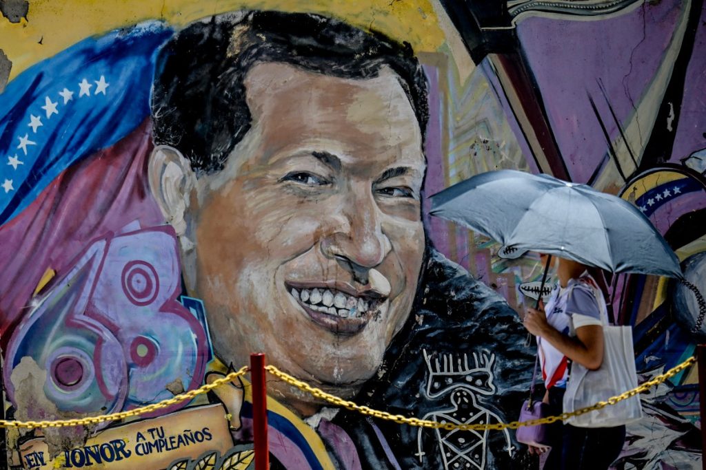 A woman covering from the sun with an umbrella arrives at the mausoleum of the former Venezuelan President Hugo Chavez during the 13th anniversary of the Venezuelan leader at the 4F barracks in the 23 de Enero neighborhood in Caracas on March 5, 2026. (Photo by Juan BARRETO / AFP)