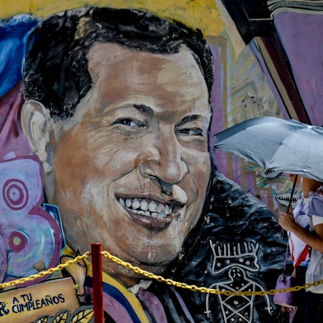 A woman covering from the sun with an umbrella arrives at the mausoleum of the former Venezuelan President Hugo Chavez during the 13th anniversary of the Venezuelan leader at the 4F barracks in the 23 de Enero neighborhood in Caracas on March 5, 2026. (Photo by Juan BARRETO / AFP)