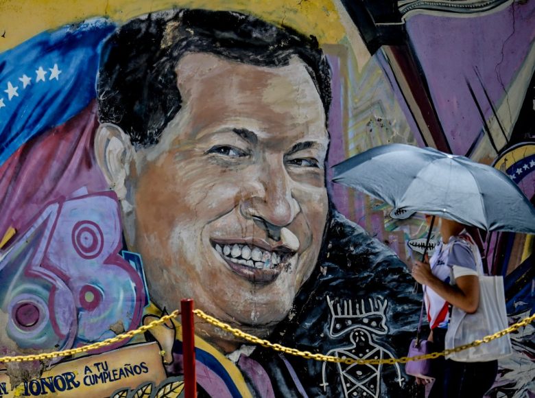 A woman covering from the sun with an umbrella arrives at the mausoleum of the former Venezuelan President Hugo Chavez during the 13th anniversary of the Venezuelan leader at the 4F barracks in the 23 de Enero neighborhood in Caracas on March 5, 2026. (Photo by Juan BARRETO / AFP)