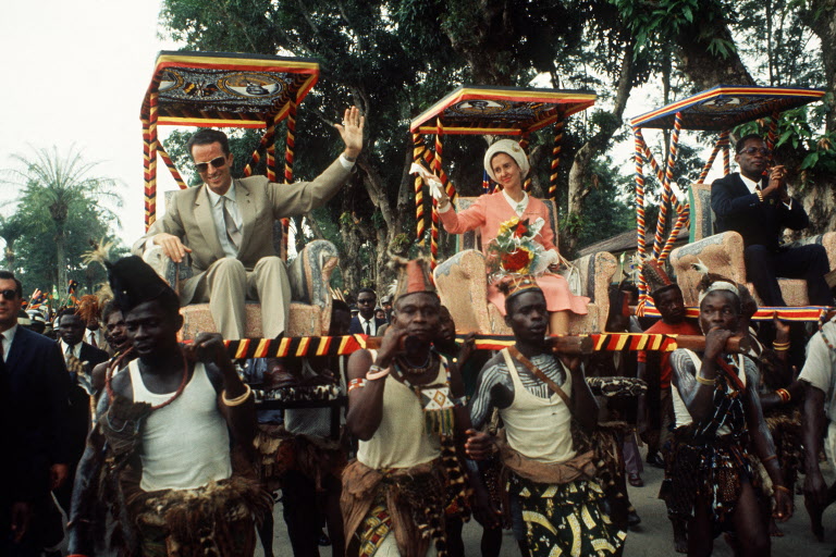 King Baudouin of Belgium and his wife Queen Fabiola wave to wellwishers as they are carried 26 June 1970 in the armchairs during their trip to Kinshasa, in Congo. (Photo by AFP)
