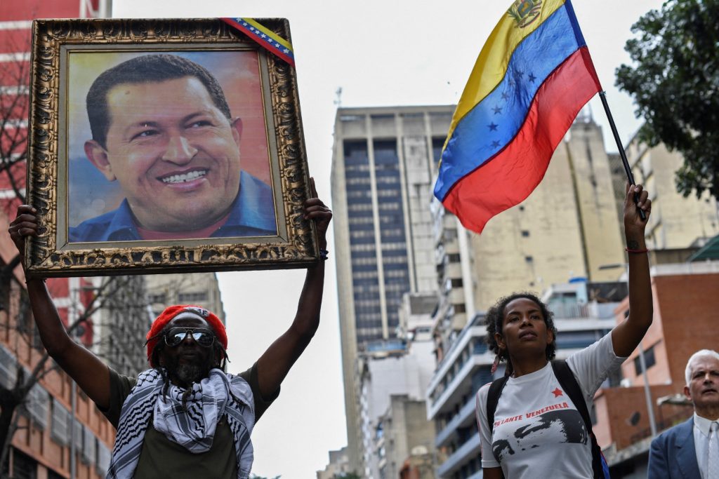 Supporters of Venezuelan President Nicolas Maduro hold a portrait of late Venezuelan President Hugo Chavez and a Venezuelan national flag during a march in solidarity with the social movements that have exploded in Latin American countries in the last days, in Caracas, on October 24, 2019. Thousands of government supporters paraded down a main avenue to show their support for the protests in Chile, Honduras, Ecuador, and to support Bolivian President Evo Morales. (Photo by Yuri CORTEZ / AFP)