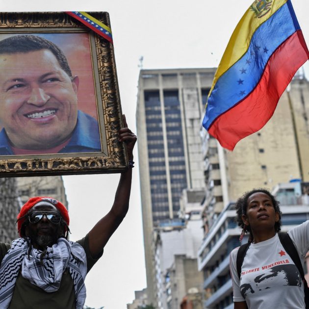 Supporters of Venezuelan President Nicolas Maduro hold a portrait of late Venezuelan President Hugo Chavez and a Venezuelan national flag during a march in solidarity with the social movements that have exploded in Latin American countries in the last days, in Caracas, on October 24, 2019. Thousands of government supporters paraded down a main avenue to show their support for the protests in Chile, Honduras, Ecuador, and to support Bolivian President Evo Morales. (Photo by Yuri CORTEZ / AFP)