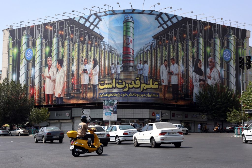 Iranians drive next to a billboard displaying pictures of nuclear scientists, centrifuges and a sentence reading in Farsi: " Science is the power", at the Enqelab square in Tehran, on August 29, 2025. Iran said on August 29 the decision by European powers to trigger a mechanism reimposing sanctions under a moribund 2015 nuclear deal would undermine Tehran's cooperation with the United Nations nuclear watchdog. Britain, France and Germany -- known as the E3 -- triggered the so-called "snapback" mechanism after weeks of warnings, citing Iran's continued non-compliance with its commitments under the 2015 nuclear agreement (Photo by AFP)
