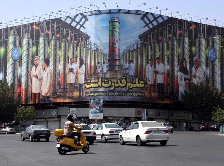 Iranians drive next to a billboard displaying pictures of nuclear scientists, centrifuges and a sentence reading in Farsi: " Science is the power", at the Enqelab square in Tehran, on August 29, 2025. Iran said on August 29 the decision by European powers to trigger a mechanism reimposing sanctions under a moribund 2015 nuclear deal would undermine Tehran's cooperation with the United Nations nuclear watchdog. Britain, France and Germany -- known as the E3 -- triggered the so-called "snapback" mechanism after weeks of warnings, citing Iran's continued non-compliance with its commitments under the 2015 nuclear agreement (Photo by AFP)