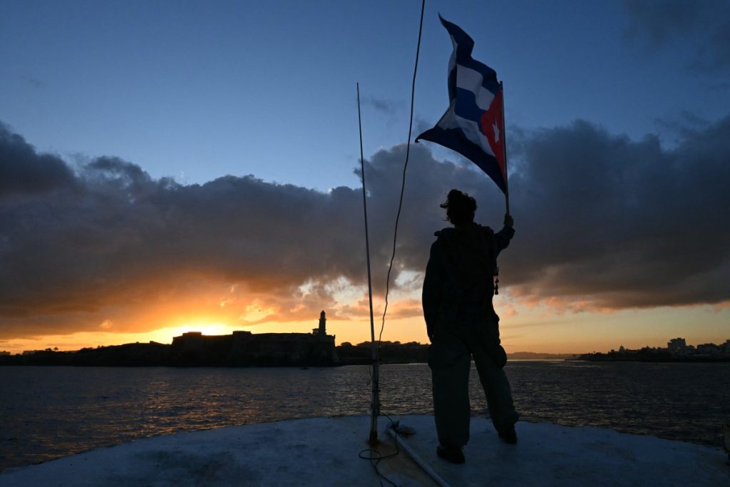 An activist waves a Cuban flag on board the vessel Maguro -- symbolically renamed "Granma 2.0" as a tribute to the yacht used by Fidel Castro's guerrilla fighters to launch their revolution in 1956 -- as it arrives from Mexico with humanitarian aid as part of the Nuestra America convoy, docking at the port of Havana on March 24, 2026. (Photo by YURI CORTEZ / AFP)