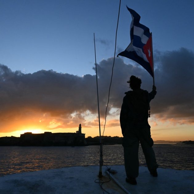 An activist waves a Cuban flag on board the vessel Maguro -- symbolically renamed "Granma 2.0" as a tribute to the yacht used by Fidel Castro's guerrilla fighters to launch their revolution in 1956 -- as it arrives from Mexico with humanitarian aid as part of the Nuestra America convoy, docking at the port of Havana on March 24, 2026. (Photo by YURI CORTEZ / AFP)