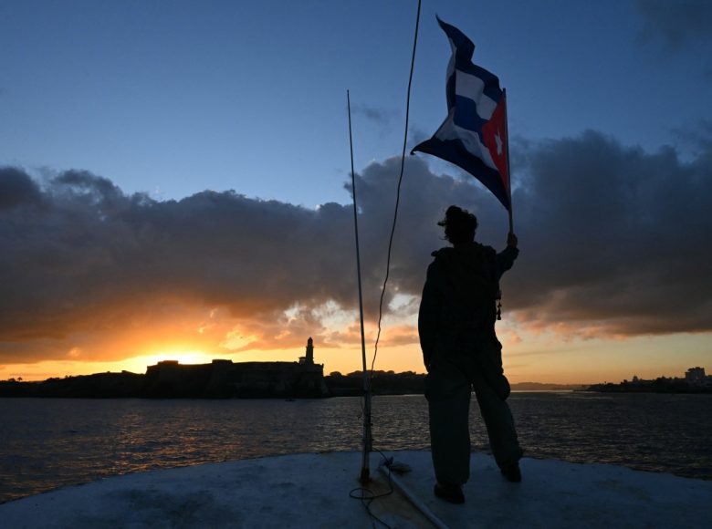 An activist waves a Cuban flag on board the vessel Maguro -- symbolically renamed "Granma 2.0" as a tribute to the yacht used by Fidel Castro's guerrilla fighters to launch their revolution in 1956 -- as it arrives from Mexico with humanitarian aid as part of the Nuestra America convoy, docking at the port of Havana on March 24, 2026. (Photo by YURI CORTEZ / AFP)