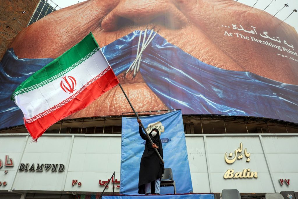 A woman waves an Iranian flag in front of an anti-US billboard referring to US President Donald Trump and the Strait of Hormuz at Valiasr Square in Tehran on May 5, 2026. Iran's chief negotiator in talks with the United States warned on May 5 that his country has "not even started" in its standoff over the Strait of Hormuz. (Photo by AFP) /