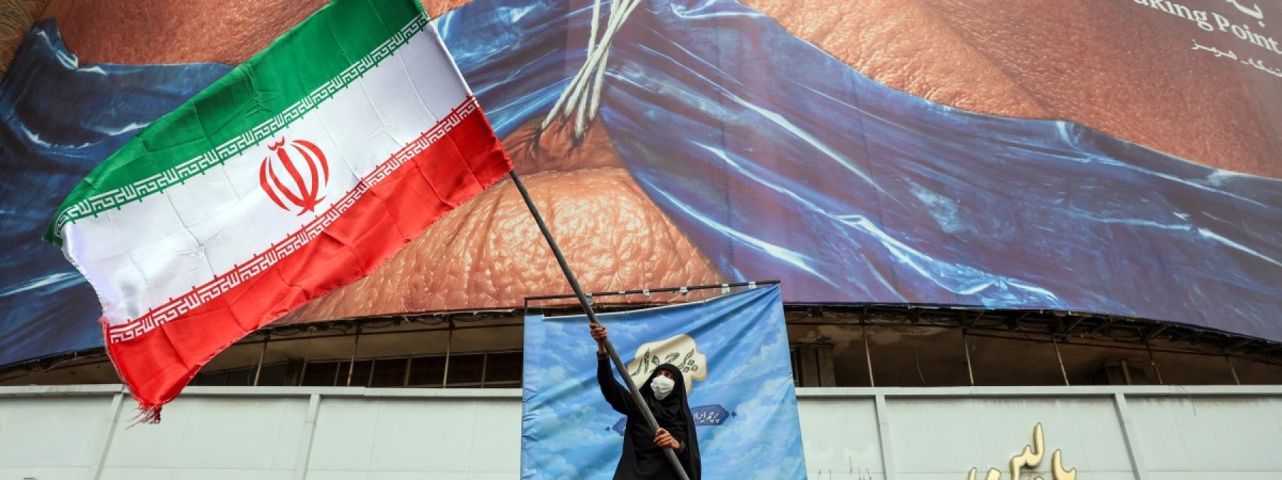 A woman waves an Iranian flag in front of an anti-US billboard referring to US President Donald Trump and the Strait of Hormuz at Valiasr Square in Tehran on May 5, 2026. Iran's chief negotiator in talks with the United States warned on May 5 that his country has "not even started" in its standoff over the Strait of Hormuz. (Photo by AFP) /