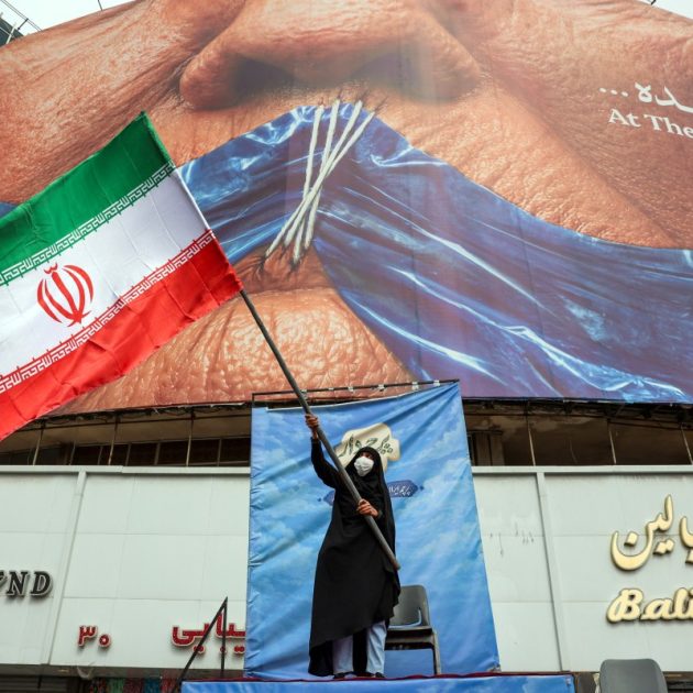 A woman waves an Iranian flag in front of an anti-US billboard referring to US President Donald Trump and the Strait of Hormuz at Valiasr Square in Tehran on May 5, 2026. Iran's chief negotiator in talks with the United States warned on May 5 that his country has "not even started" in its standoff over the Strait of Hormuz. (Photo by AFP) /