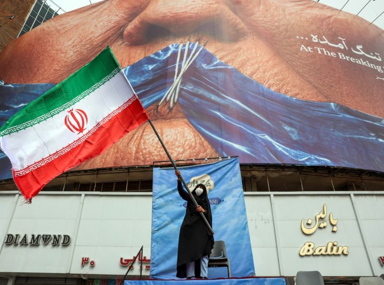 A woman waves an Iranian flag in front of an anti-US billboard referring to US President Donald Trump and the Strait of Hormuz at Valiasr Square in Tehran on May 5, 2026. Iran's chief negotiator in talks with the United States warned on May 5 that his country has "not even started" in its standoff over the Strait of Hormuz. (Photo by AFP) /