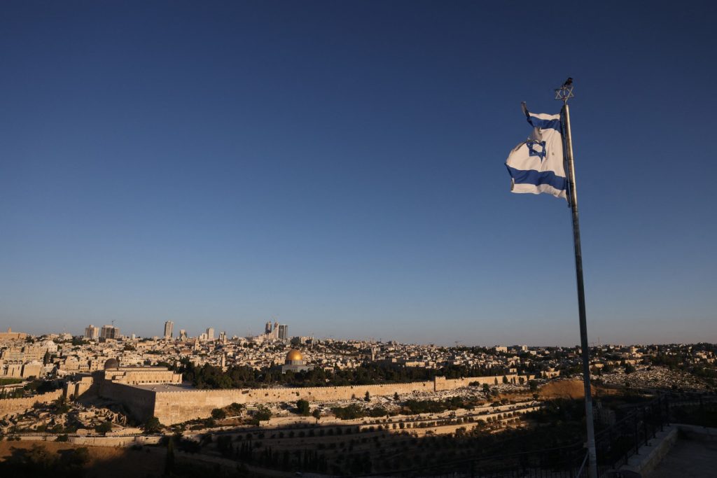 An Israeli flag flutters on the Mount of Olives as the sun rises over Jerusalem and its landmark Dome of the Rock mosque on June 13, 2025, following Israeli Prime Minister Benjamin Netanyahu's announcement that a military operation was launched against Iran and would "continue for as many days as it takes". Israel carried out strikes targeting nuclear and military sites in Iran early on June 13, after US President Donald Trump warned of a possible "massive conflict" in the region. (Photo by AHMAD GHARABLI / AFP)