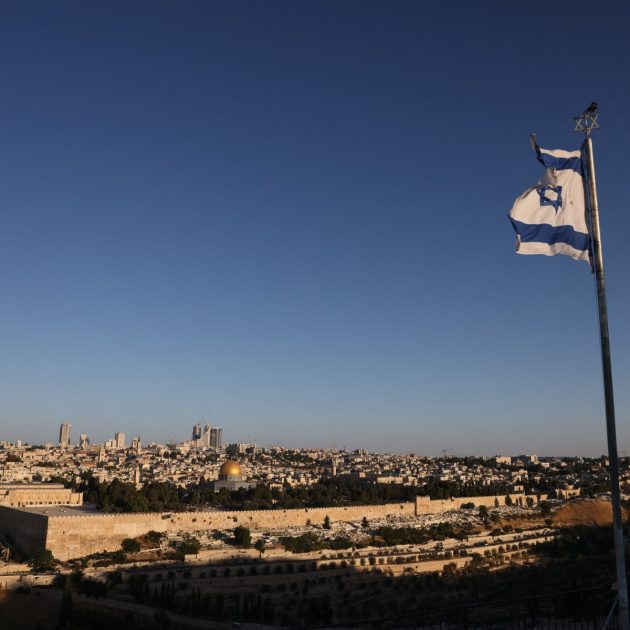 An Israeli flag flutters on the Mount of Olives as the sun rises over Jerusalem and its landmark Dome of the Rock mosque on June 13, 2025, following Israeli Prime Minister Benjamin Netanyahu's announcement that a military operation was launched against Iran and would "continue for as many days as it takes". Israel carried out strikes targeting nuclear and military sites in Iran early on June 13, after US President Donald Trump warned of a possible "massive conflict" in the region. (Photo by AHMAD GHARABLI / AFP)