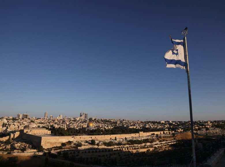 An Israeli flag flutters on the Mount of Olives as the sun rises over Jerusalem and its landmark Dome of the Rock mosque on June 13, 2025, following Israeli Prime Minister Benjamin Netanyahu's announcement that a military operation was launched against Iran and would "continue for as many days as it takes". Israel carried out strikes targeting nuclear and military sites in Iran early on June 13, after US President Donald Trump warned of a possible "massive conflict" in the region. (Photo by AHMAD GHARABLI / AFP)