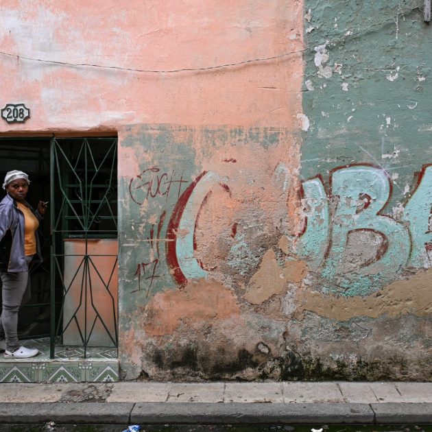 A woman peeks out from the doorway of her home next to a wall with a graffiti reading CUBA on a street in Havana, Cuba, on May 6, 2026. Havana accused Marco Rubio of "lying" after the US Secretary of State stated on May 6, 2026 that Washington had not imposed an oil embargo on Cuba and attributed the island's current energy crisis to internal mismanagement. (Photo by YAMIL LAGE / AFP)