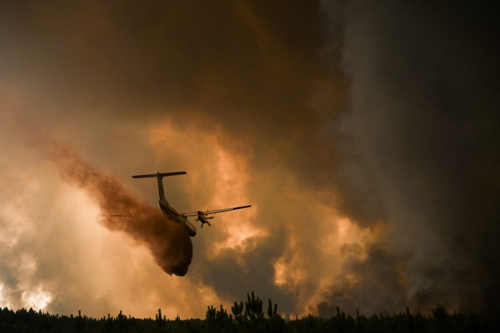 A Dash 8 firefighting aircraft sprays fire retardant over trees during a wildfire near Belin-Beliet in Gironde, southwestern France, on August 10, 2022. (Photo by Philippe LOPEZ / AFP)