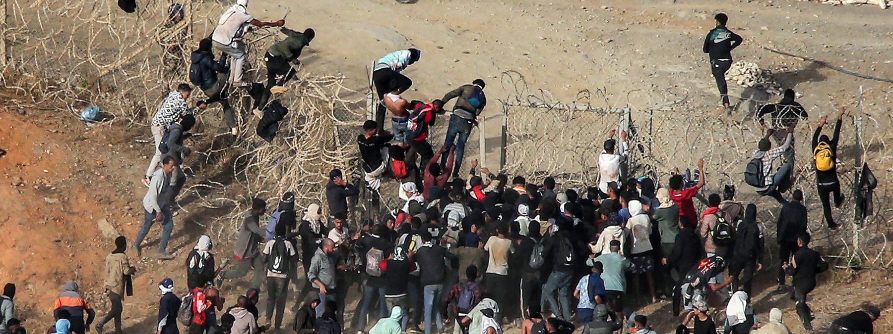 Migrants storm a barbed-wire fence as they attempt to cross the land border with Spain's African enclave of Ceuta near Fnideq in northern Morocco on September 15, 2024. (Photo by AFP)