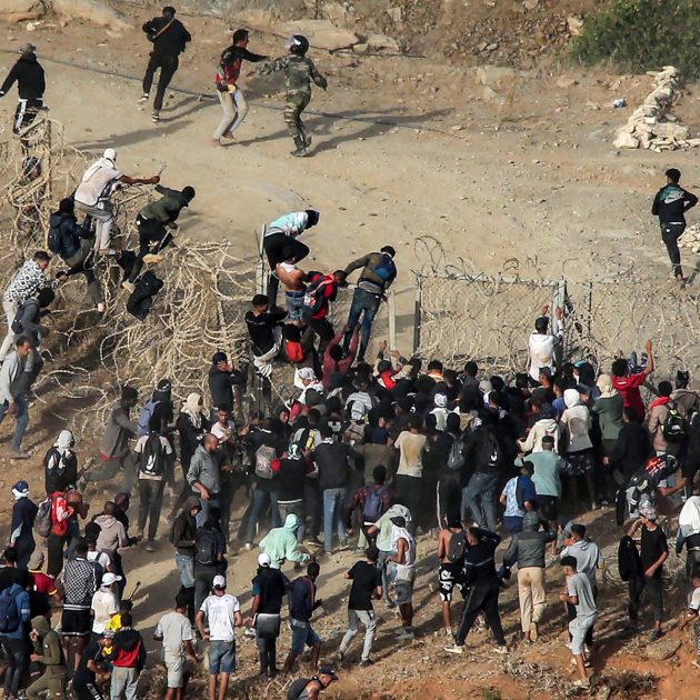 Migrants storm a barbed-wire fence as they attempt to cross the land border with Spain's African enclave of Ceuta near Fnideq in northern Morocco on September 15, 2024. (Photo by AFP)