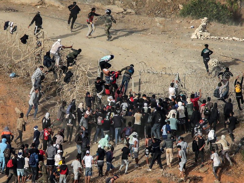Migrants storm a barbed-wire fence as they attempt to cross the land border with Spain's African enclave of Ceuta near Fnideq in northern Morocco on September 15, 2024. (Photo by AFP)