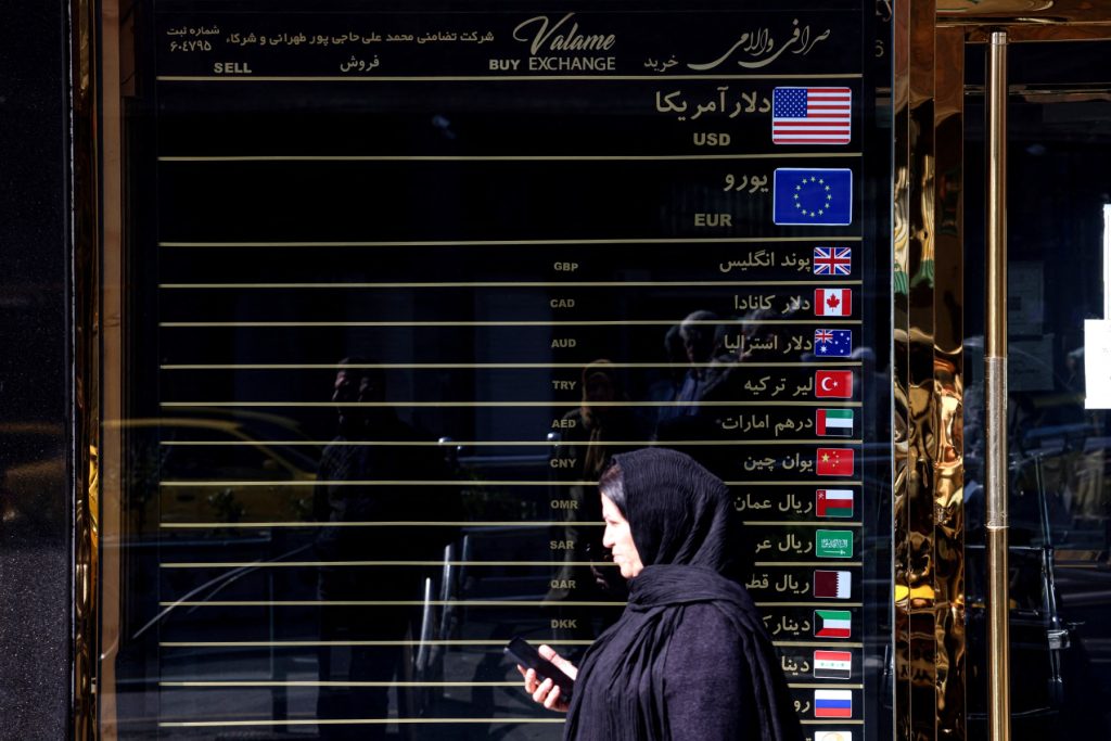 Iranian women walks In front of a currency exchange booth, in the capital Tehran on February 22, 2026. Iran is seeking to negotiate an end to sanctions that have proven to be a massive drag on its economy, which played a role in sparking anti-government protests in December 2025. (Photo by ATTA KENARE / AFP)