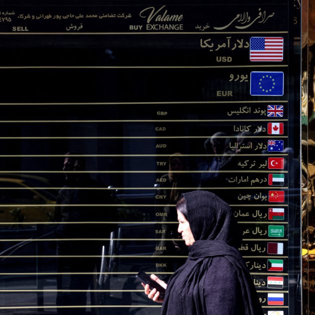 Iranian women walks In front of a currency exchange booth, in the capital Tehran on February 22, 2026. Iran is seeking to negotiate an end to sanctions that have proven to be a massive drag on its economy, which played a role in sparking anti-government protests in December 2025. (Photo by ATTA KENARE / AFP)
