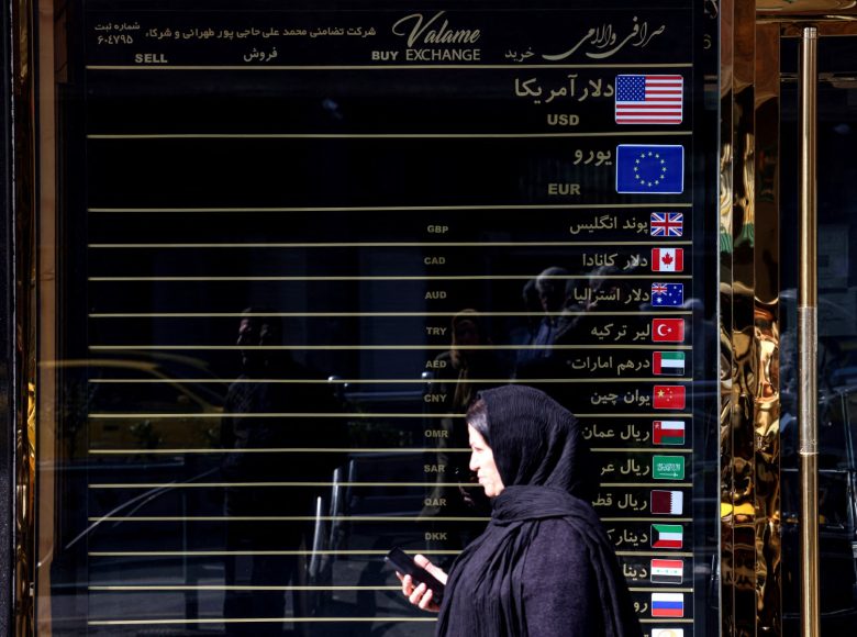 Iranian women walks In front of a currency exchange booth, in the capital Tehran on February 22, 2026. Iran is seeking to negotiate an end to sanctions that have proven to be a massive drag on its economy, which played a role in sparking anti-government protests in December 2025. (Photo by ATTA KENARE / AFP)