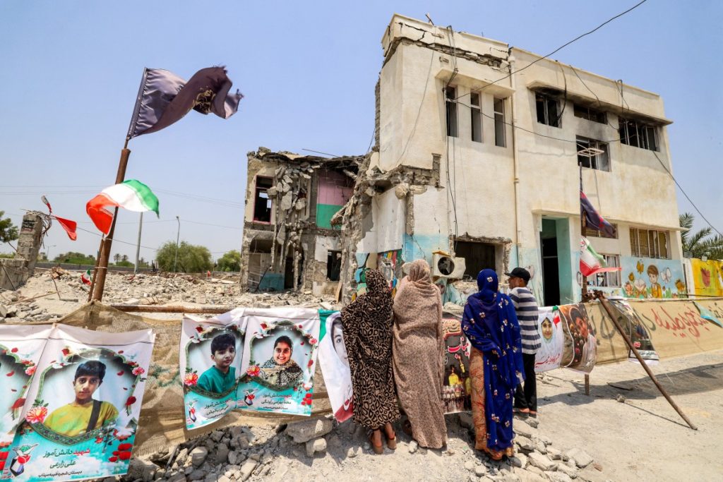 People stand near the building of the destroyed Shajareh Tayyebeh primary school in Minab in Irans Hormozgan province on August 10, 2026. In the early hours of the US and Israel's war with Iran in late February, the school in southern Iran was hit, killing at least 73 boys and 47 girls among more than 150 fatalities, Iranian officials had said. (Photo by ATTA KENARE / AFP) /