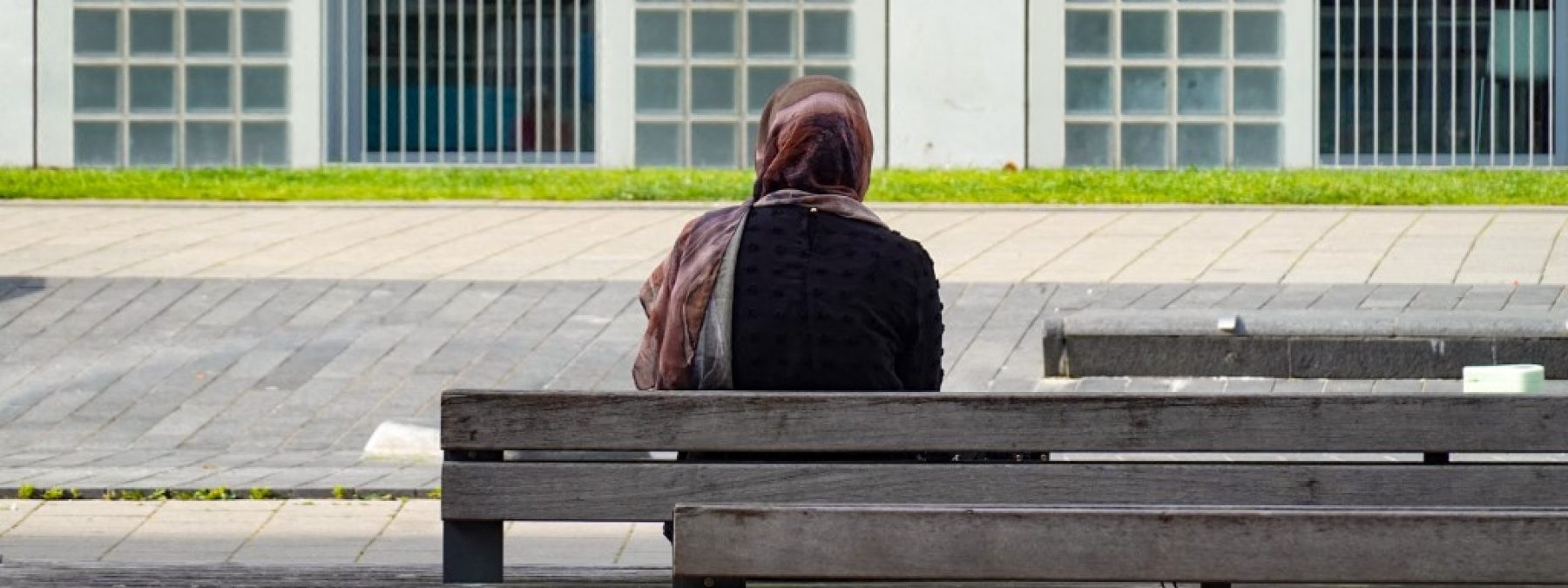 A woman with a headscarf sits alone on a bench, facing a modern building facade in Stuttgart, Baden-Wuerttemberg, Germany, on June 21, 2025. (Photo by Michael Nguyen/NurPhoto) (Photo by Michael Nguyen / NurPhoto via AFP)
