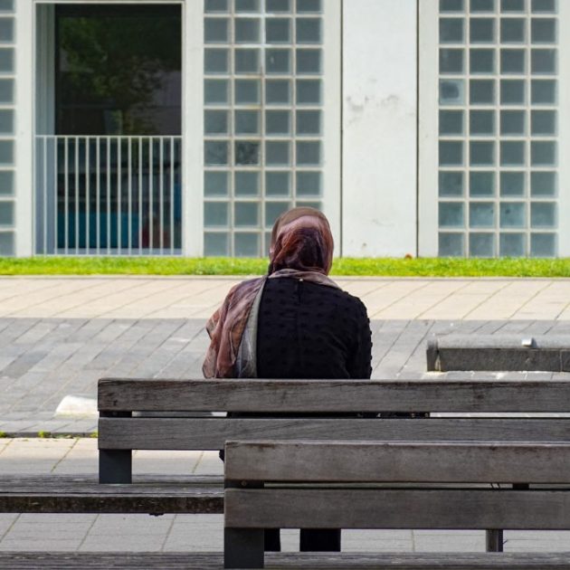 A woman with a headscarf sits alone on a bench, facing a modern building facade in Stuttgart, Baden-Wuerttemberg, Germany, on June 21, 2025. (Photo by Michael Nguyen/NurPhoto) (Photo by Michael Nguyen / NurPhoto via AFP)