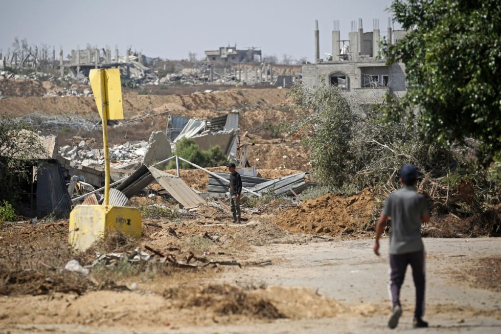 Palestinians walk past a concrete block marking the 'Yellow Line' drawn by the Israeli military in the east of Deir al-Balah, central Gaza Strip on July 22, 2026, as violence has continued in Gaza despite the ceasefire. Gaza remains gripped by daily violence, with both the Israeli military and Hamas accusing one another of violating the truce in effect since October 10. The war flattened swathes of the territory, displaced most of the population at least once, and left hundreds of thousands of people living in tents and temporary shelters. (Photo by Eyad Baba / AFP)