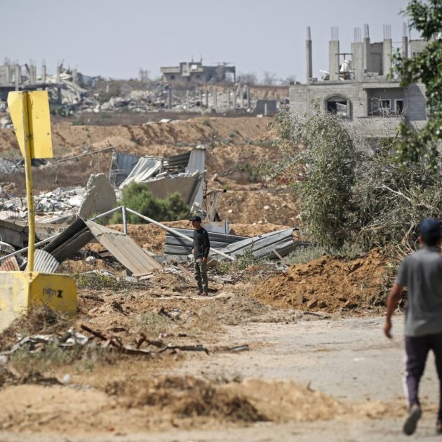 Palestinians walk past a concrete block marking the 'Yellow Line' drawn by the Israeli military in the east of Deir al-Balah, central Gaza Strip on July 22, 2026, as violence has continued in Gaza despite the ceasefire. Gaza remains gripped by daily violence, with both the Israeli military and Hamas accusing one another of violating the truce in effect since October 10. The war flattened swathes of the territory, displaced most of the population at least once, and left hundreds of thousands of people living in tents and temporary shelters. (Photo by Eyad Baba / AFP)