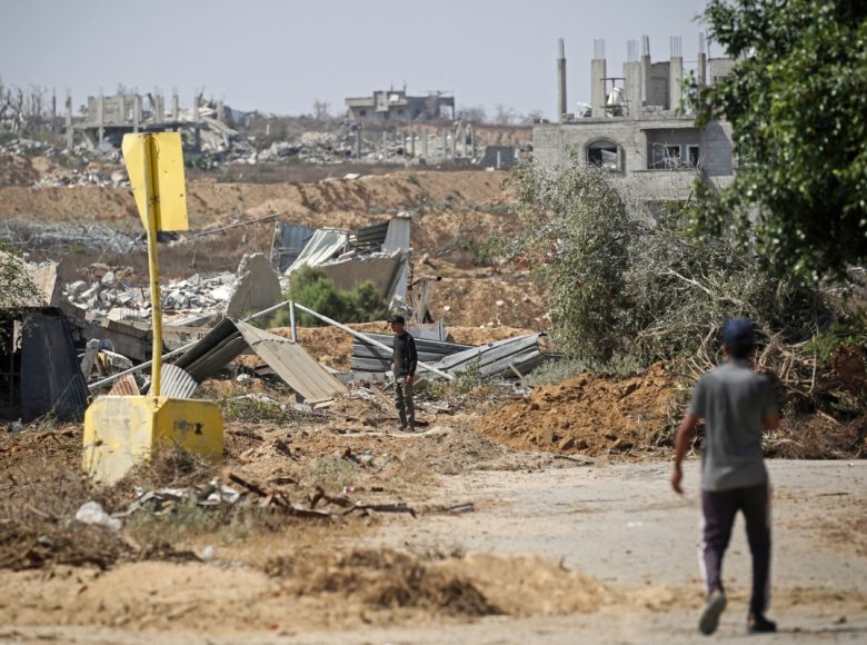 Palestinians walk past a concrete block marking the 'Yellow Line' drawn by the Israeli military in the east of Deir al-Balah, central Gaza Strip on July 22, 2026, as violence has continued in Gaza despite the ceasefire. Gaza remains gripped by daily violence, with both the Israeli military and Hamas accusing one another of violating the truce in effect since October 10. The war flattened swathes of the territory, displaced most of the population at least once, and left hundreds of thousands of people living in tents and temporary shelters. (Photo by Eyad Baba / AFP)